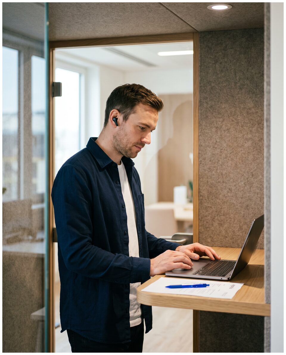 Illustration : un responsable de clientèle dans une cabine téléphonique de bureau, un écouteur à l’oreille, rédige une réponse sur un ordinateur portable.